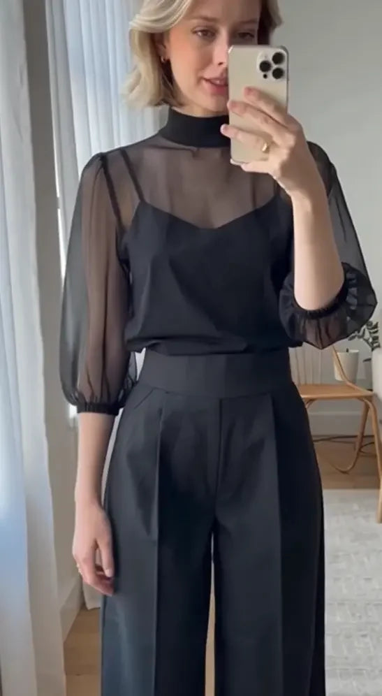 Woman in a black sheer blouse and wide-leg trousers, mirror selfie