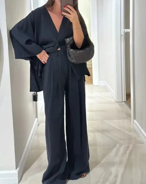Woman in a black satin wrap top and wide-leg trousers, mirror selfie
