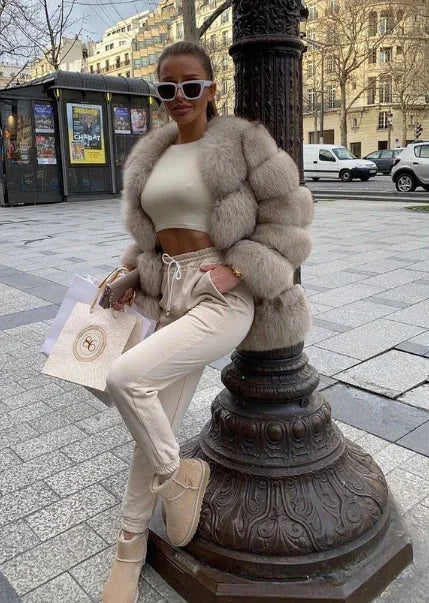 Woman in a cream faux fur jacket and white joggers on a city street