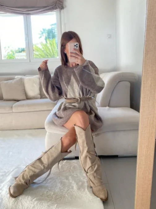 Woman in a grey knit sweater dress with a belt and beige knee-high boots